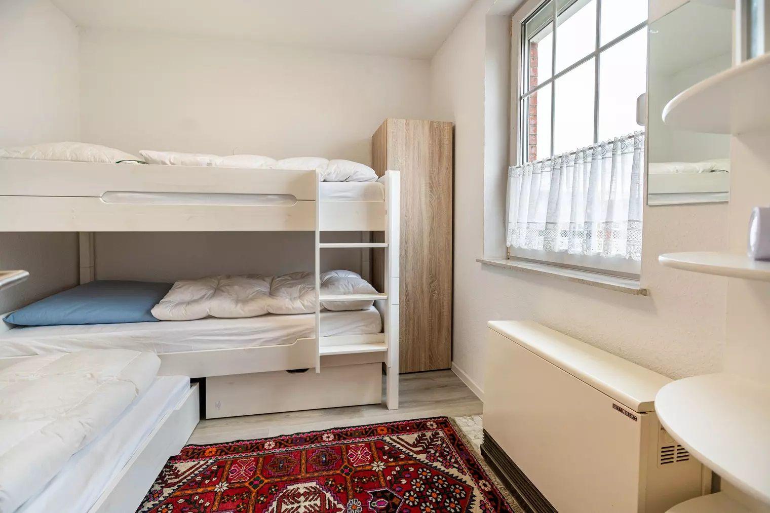 Zimmer mit Doppelstockbett, Kleiderschrank und Fenster mit Vorhang.