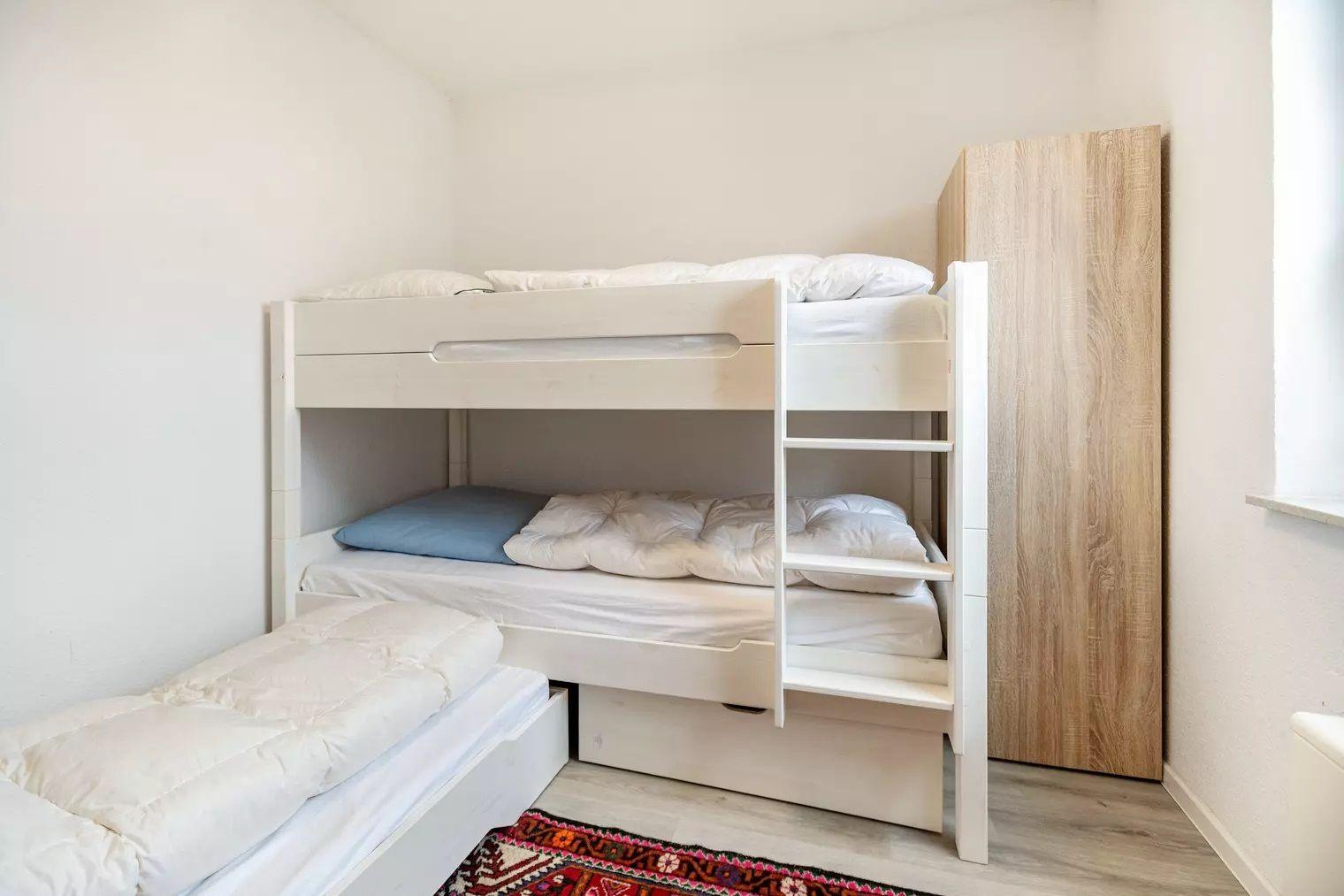 Zimmer mit Doppelstockbett, Schlafcouch und Holzschrank.