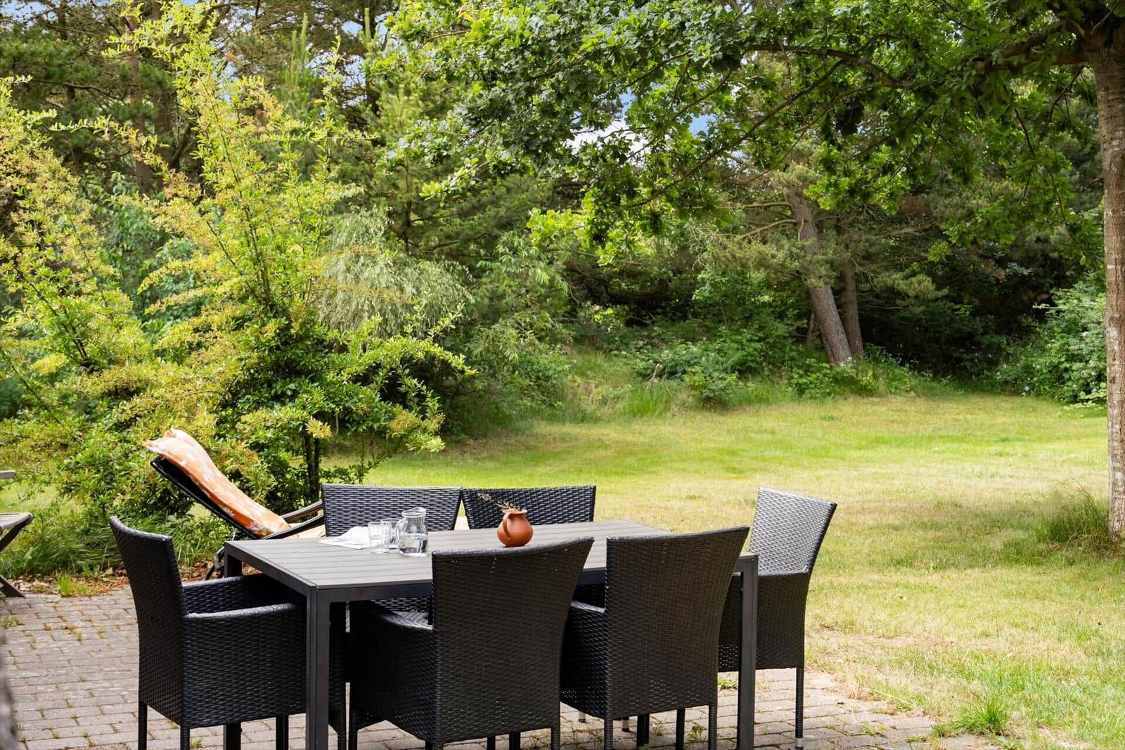 Terrasse mit Tisch, Stühlen und Liegestuhl im Grünen.