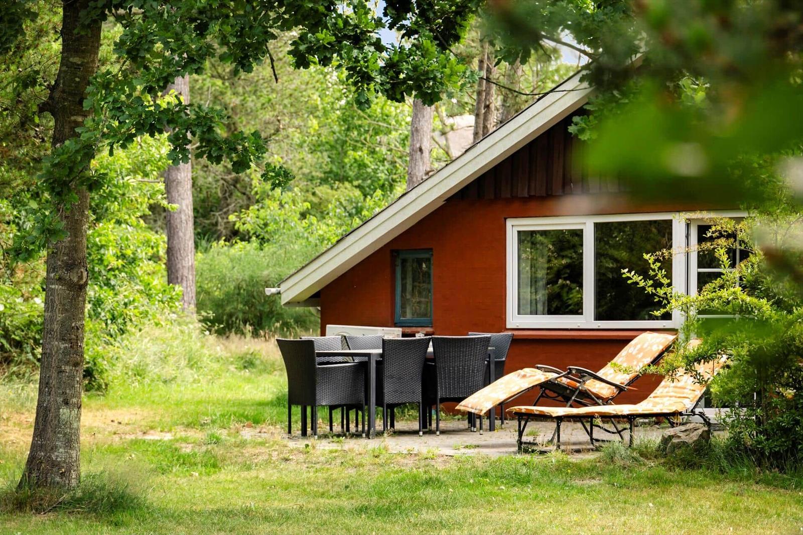 Rotes Holzhaus mit Terrasse, Tisch, Stühlen und Liegestühlen im Grünen.