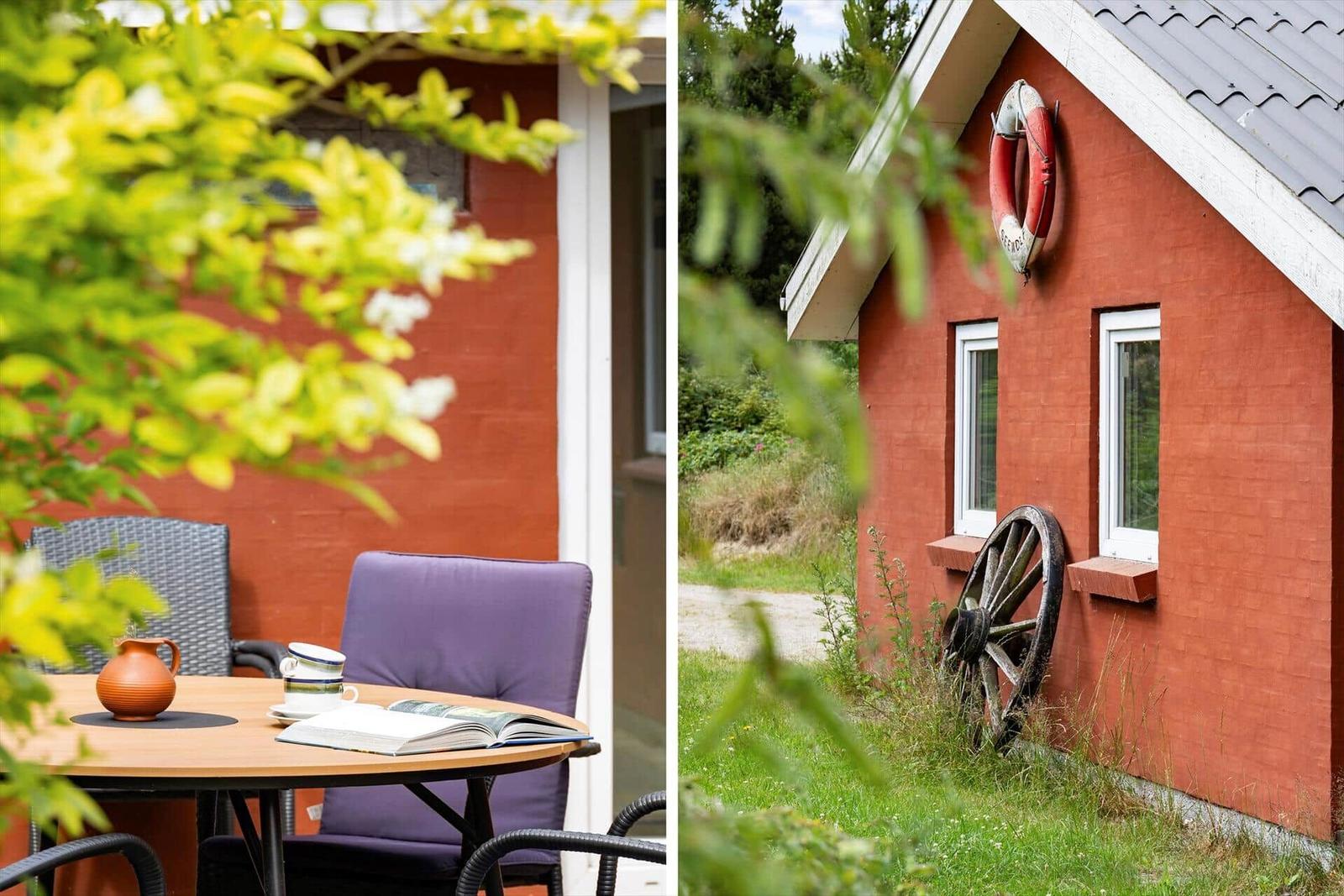 Roter Holzhaus mit Außentisch und Stuhl, Rettungsring und altes Rad an der Wand.