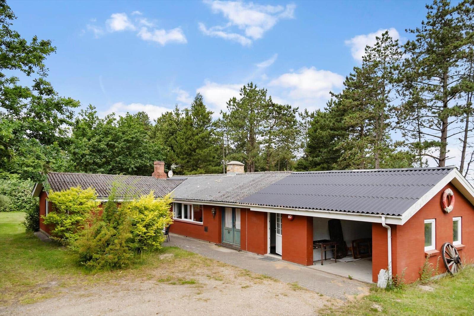 Rotes Haus mit Garage und Garten, umgeben von Bäumen unter blauem Himmel.
