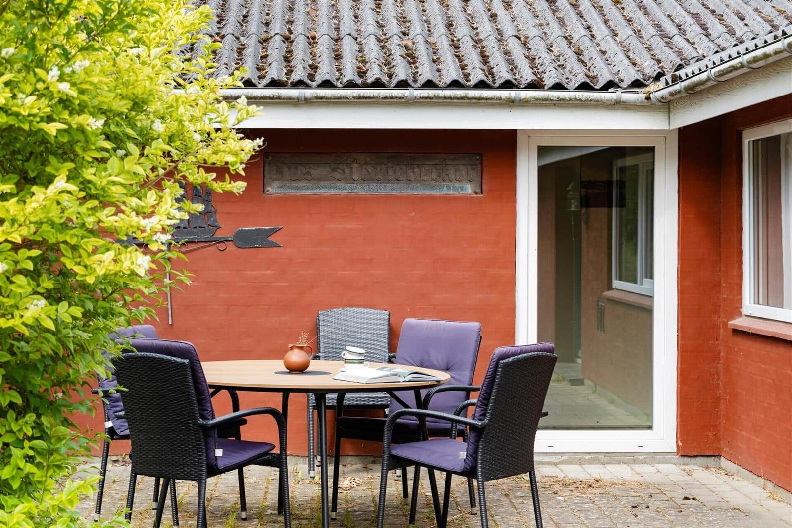 Roter Hauswände mit Terrasse, Tisch und Stühlen. Pflanzen und Dachziegel sind sichtbar.