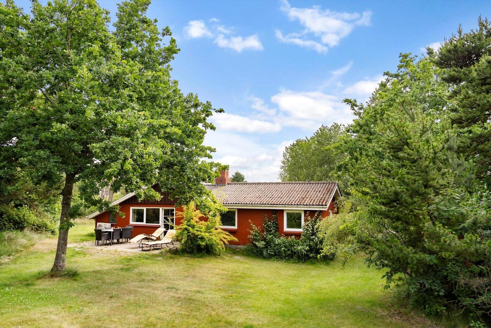 Rotes Haus mit Garten, Terrasse und Grillplatz unter Bäumen.