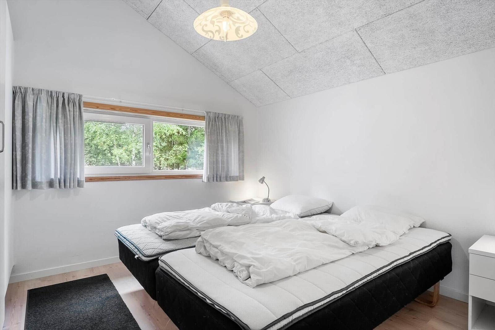 Schlafzimmer mit Doppelbett, Fenster und Deckenleuchte.