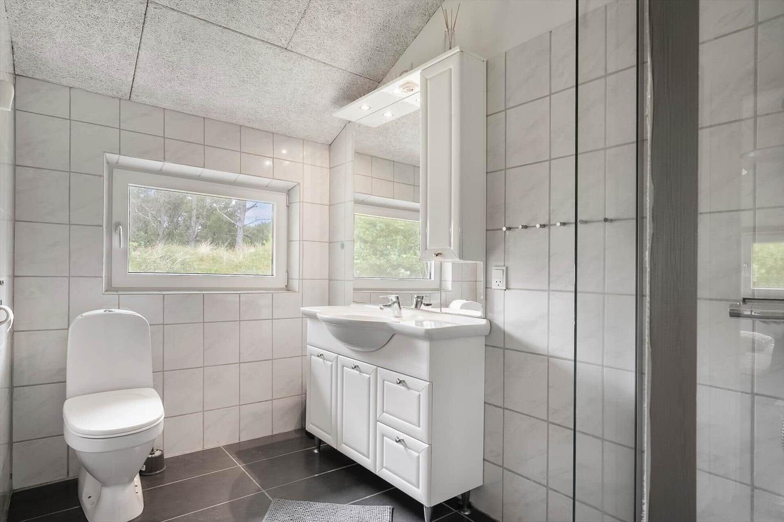 Badezimmer mit Toilette, Waschbecken und Dusche. Fenster mit Blick auf Grün.