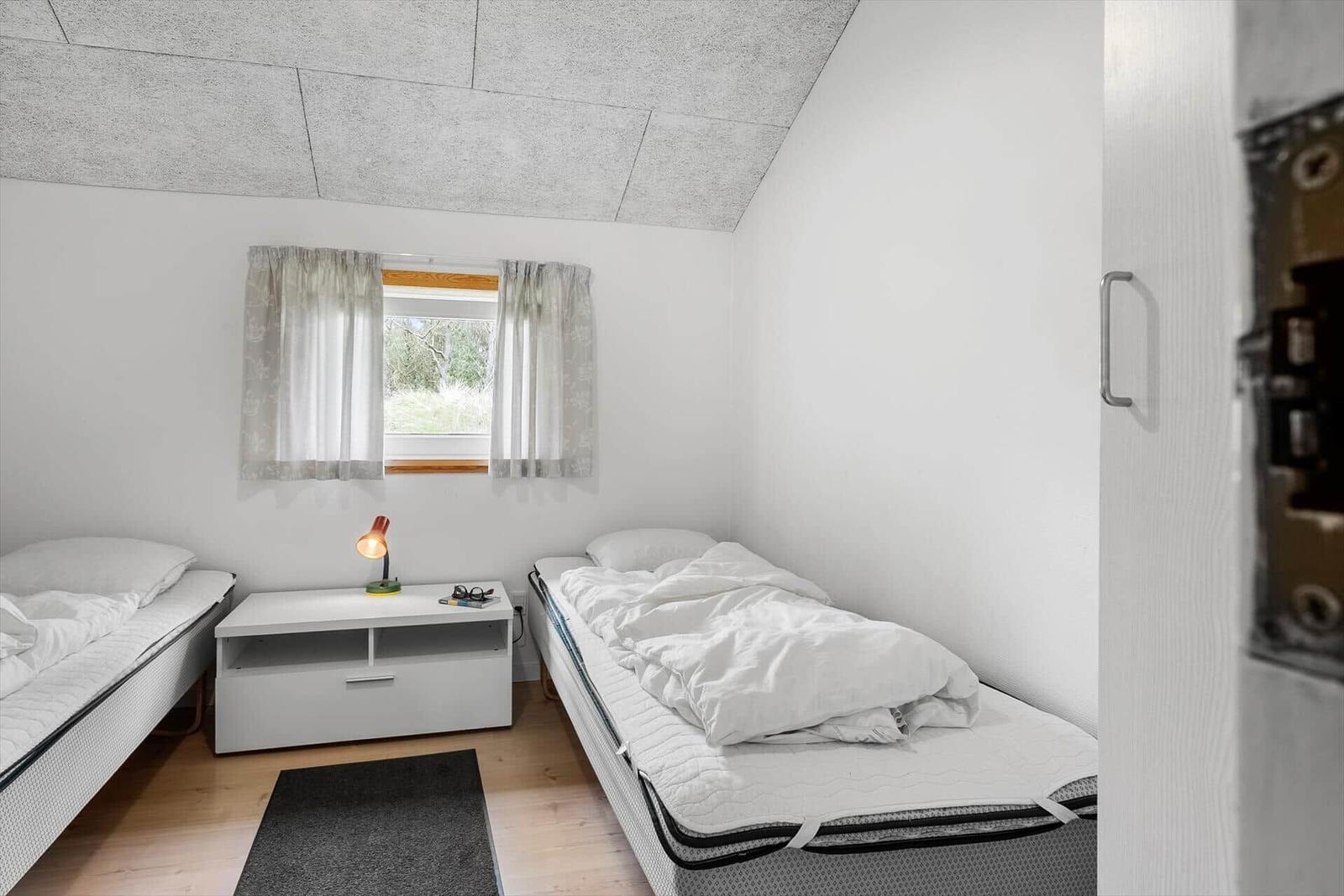 Zwei Betten, Nachttisch mit Lampe und Fenster mit Vorhängen.