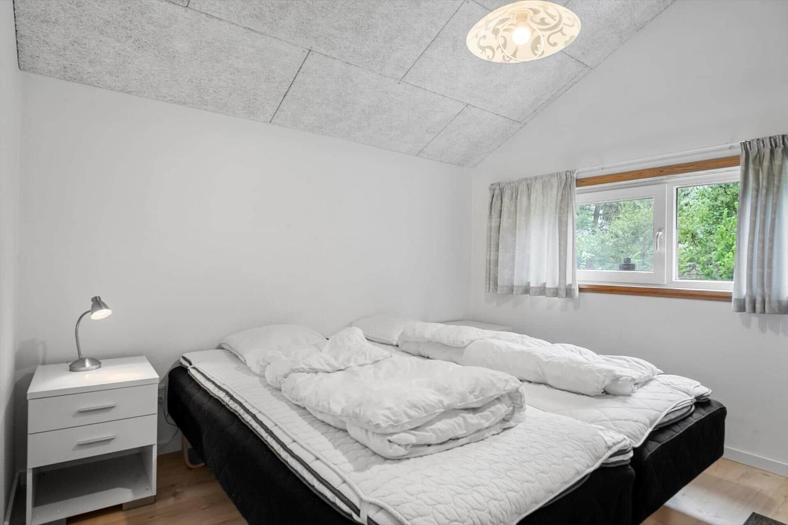 Schlafzimmer mit Doppelbett, Nachttisch und Fenster mit Blick auf Grün.