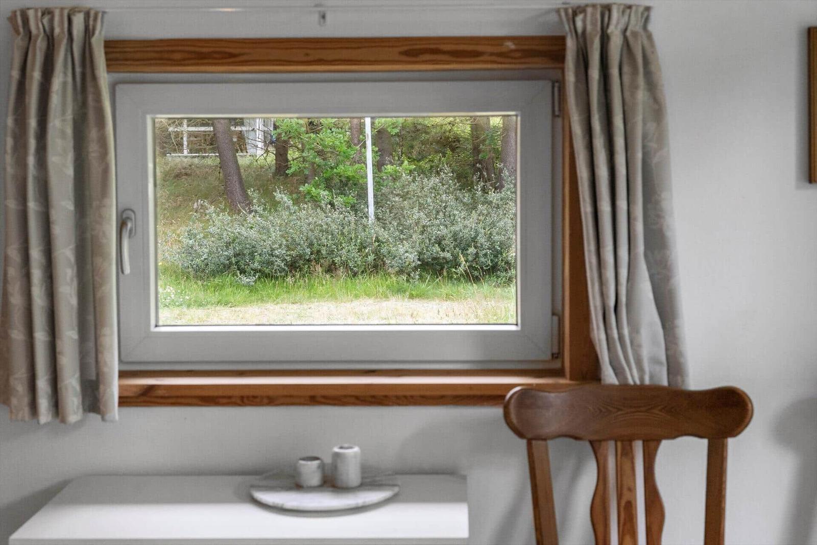 Ein Fenster mit Holzrahmen zeigt einen Blick in einen bewaldeten Bereich.