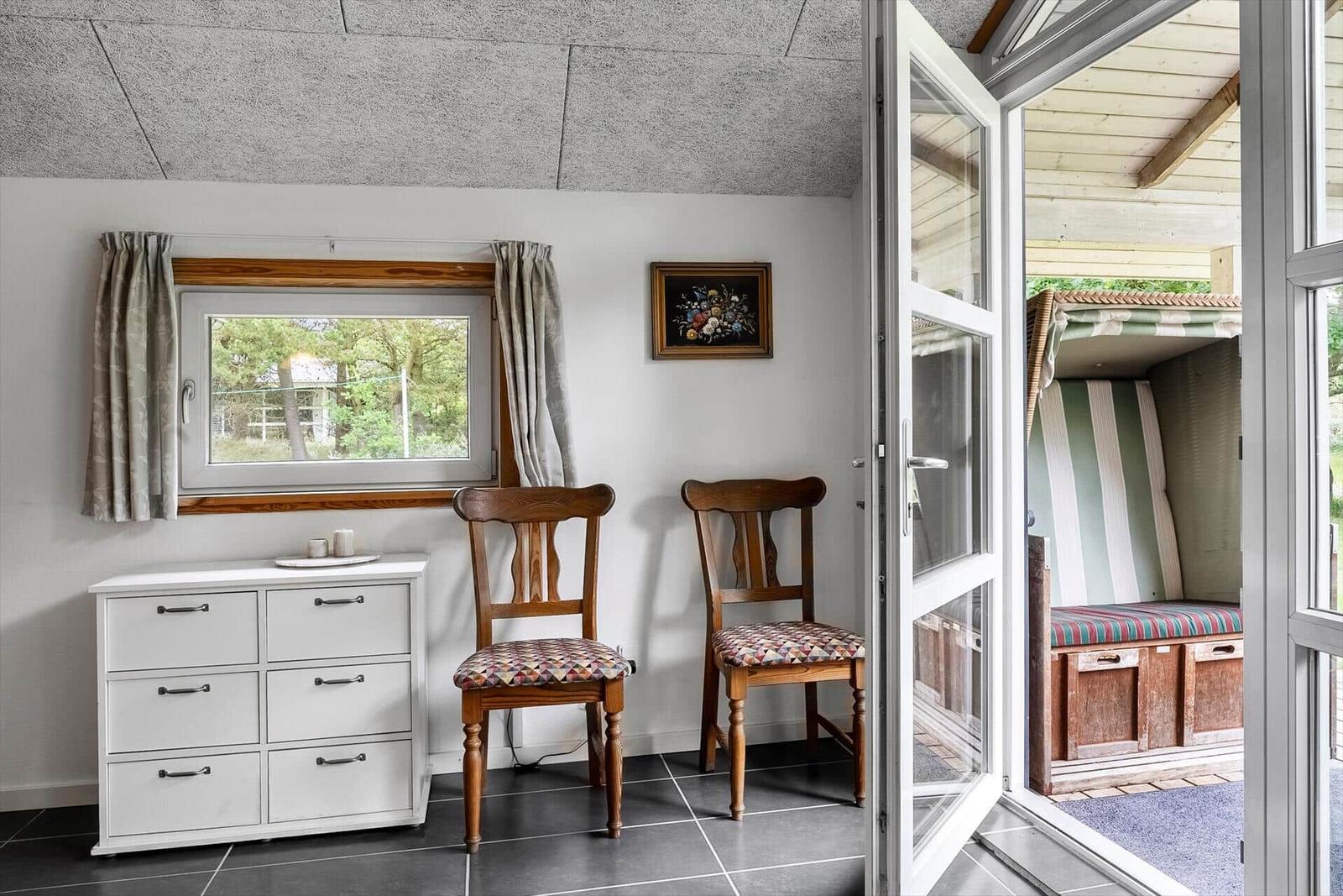 Raum mit zwei Stühlen, Schrank und Fenster. Durch Glastür Blick auf Strandkorb.