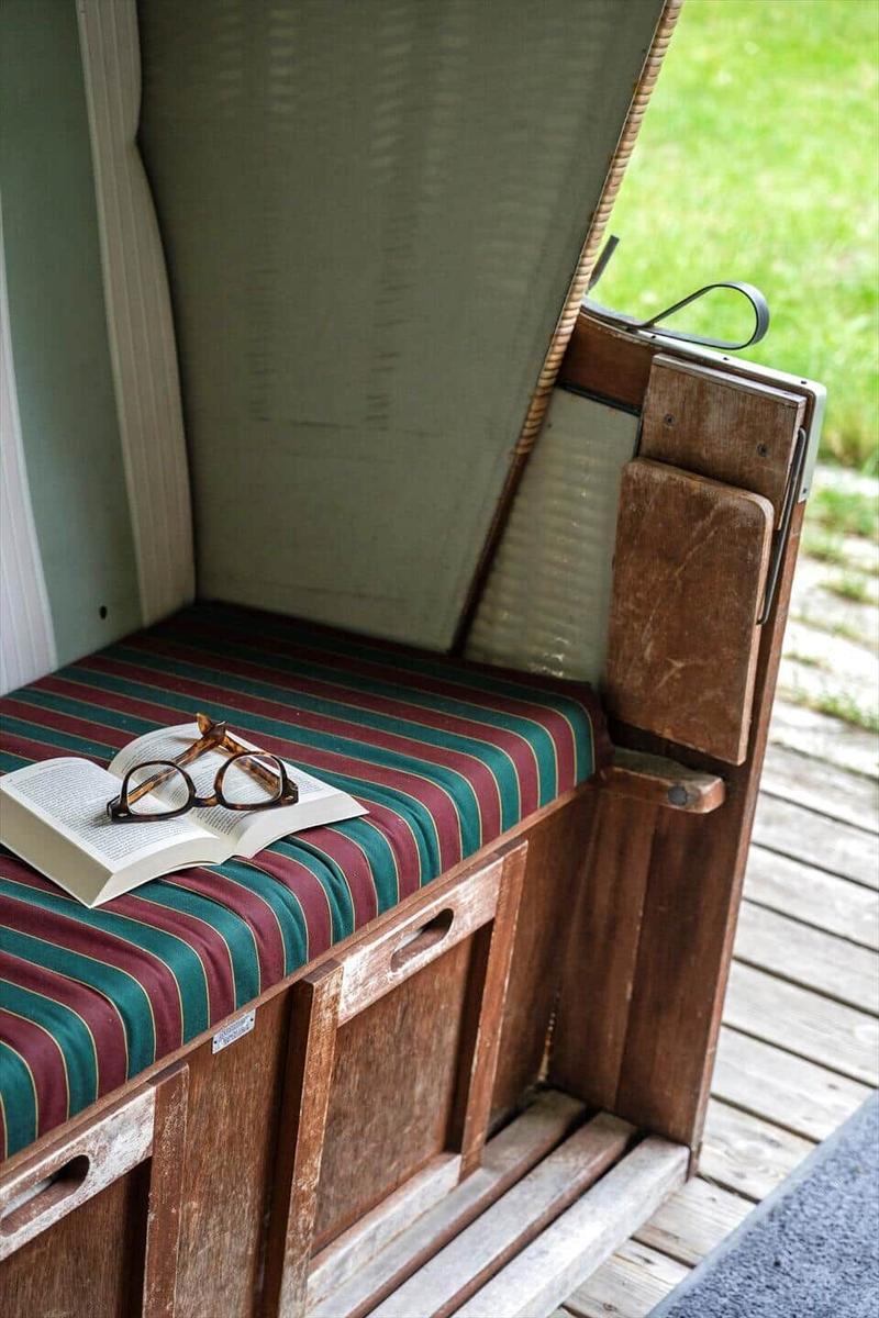 Holzbank mit gestreifter Sitzfläche und offenes Buch mit Brille.
