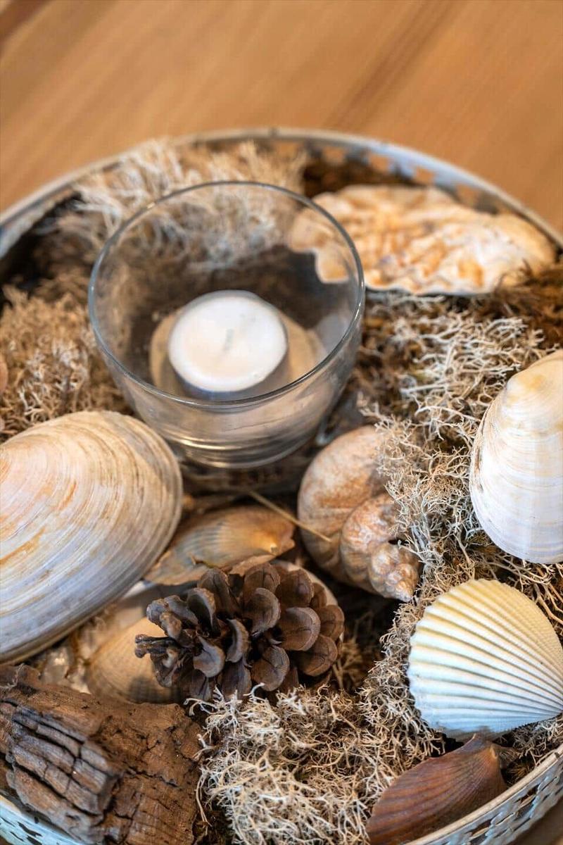 Dekorative Schale mit Muscheln, Kiefernzapfen und Kerze auf Holztisch
