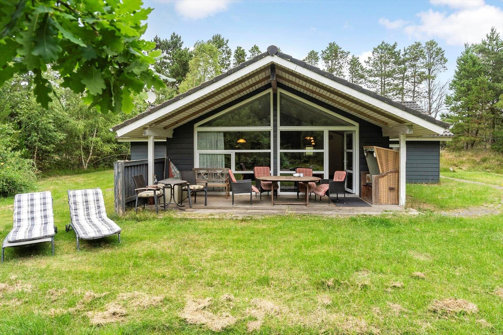 Haus mit Terrasse, Garten und Liegestühlen. Blick in Wohnbereich durch große Fenster.