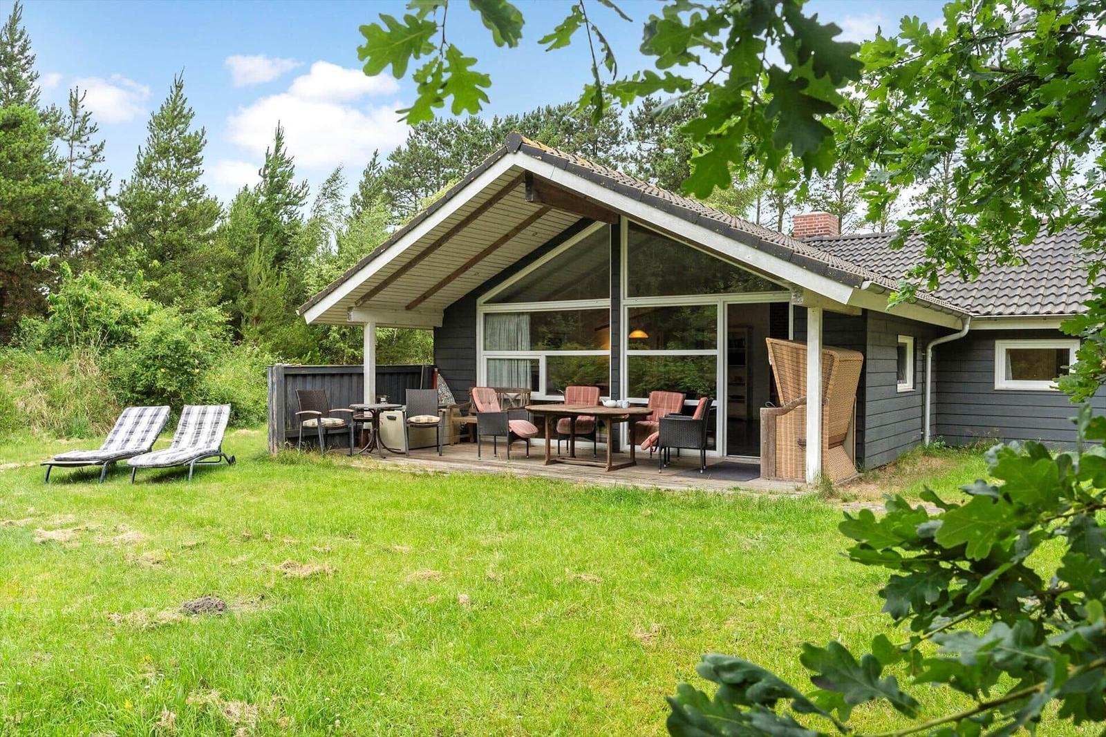 Ein Haus mit Terrasse, Garten und Liegestühlen unter Bäumen.