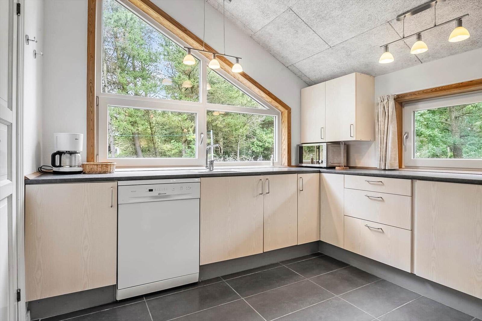 Küche mit Holzschränken, Spüle, Waschmaschine und Fenster zur Natur.