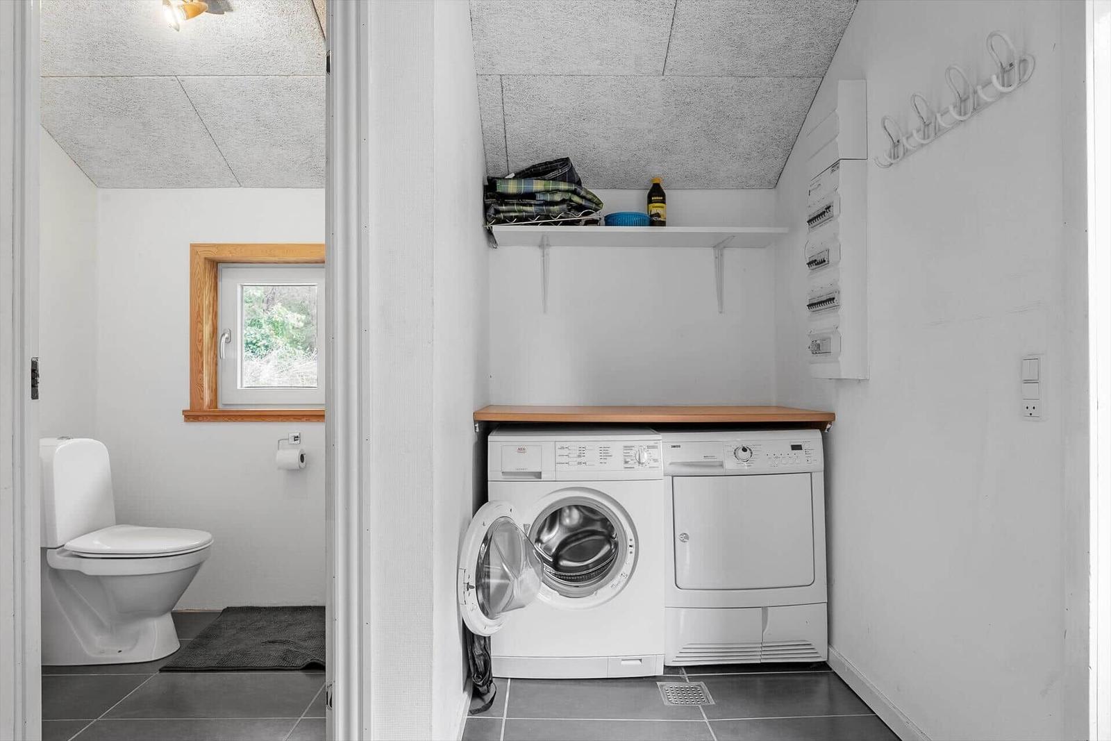 Waschraum mit Waschmaschine und Trockner. Nebenraum mit Toilette und Fenster.