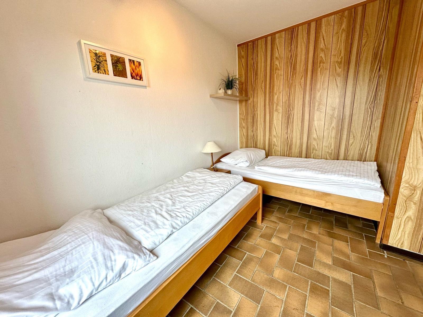 Zwei Betten mit weißen Laken, Holzwand und Fliesenboden.