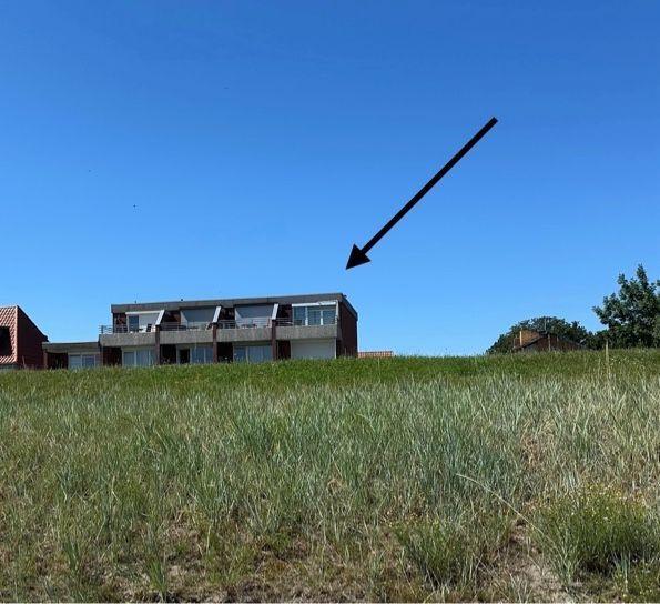 Modernes Gebäude mit Balkonen auf grünem Hang unter blauem Himmel