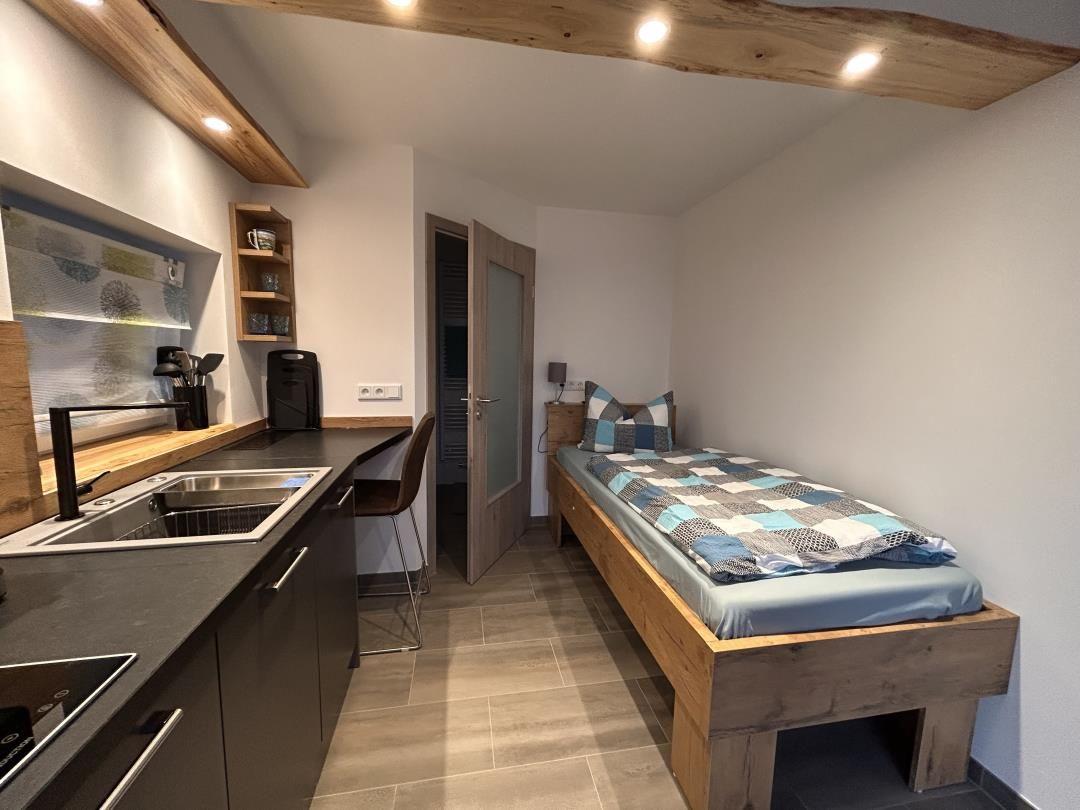 Schlafzimmer mit Bett, Küchenzeile und Holzbalken an der Decke.