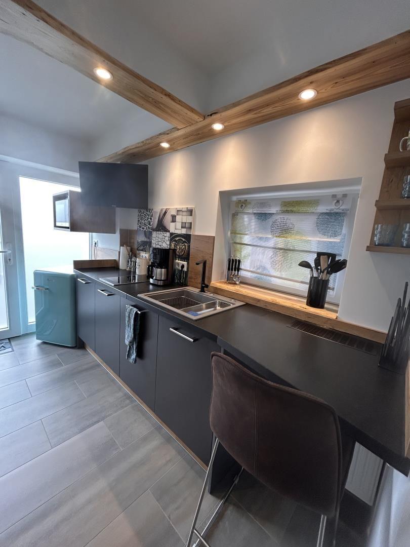 Moderne Küche mit dunklen Schränken, Holzbalken und Fenster mit Jalousie.