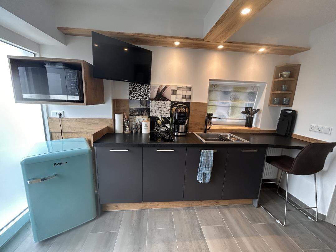 Küche mit dunklen Schränken, Küchenzeile und Kücheninsel mit Stuhl.