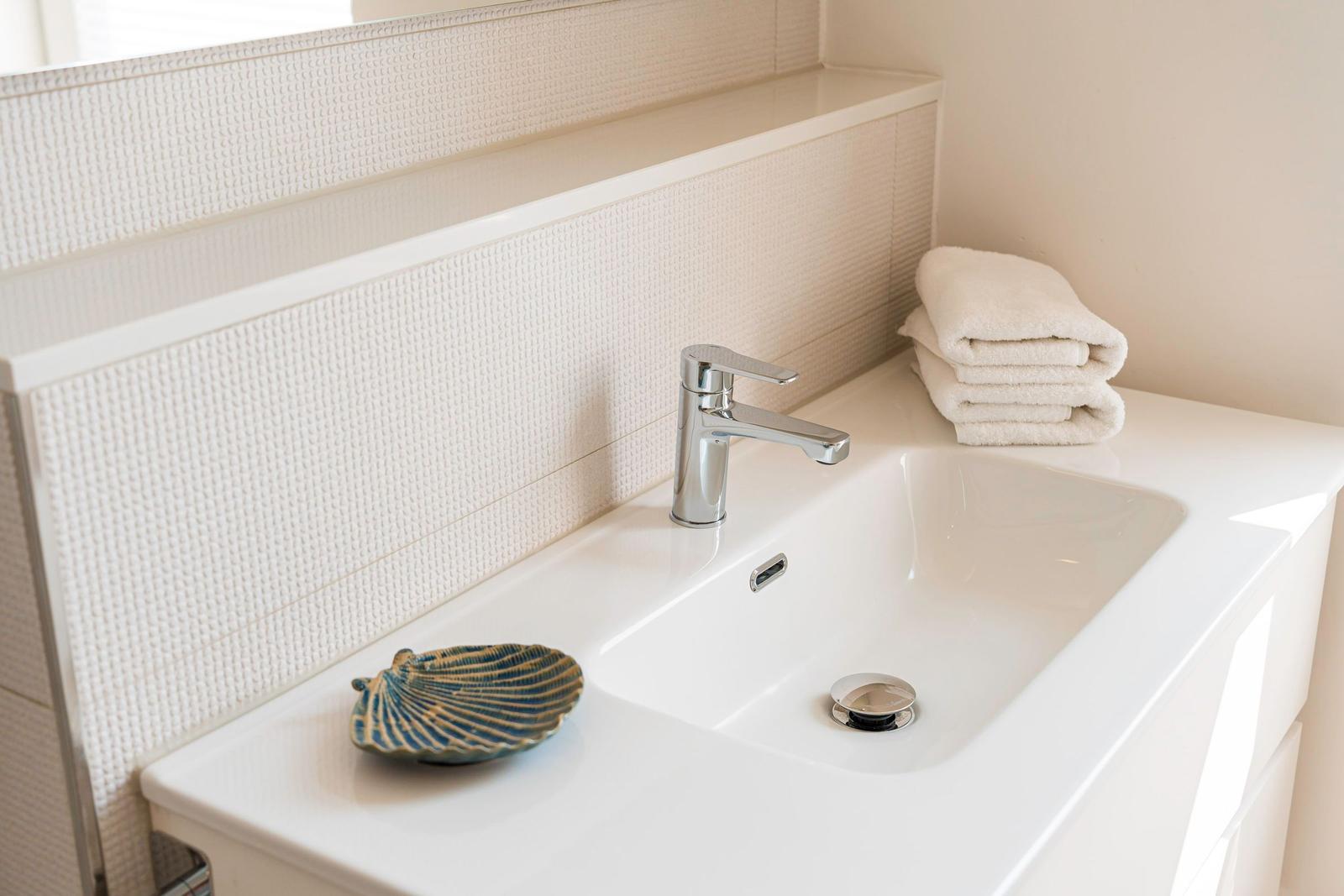 Waschbecken mit Chromhahn, Handtücher und Schale auf der Arbeitsfläche.