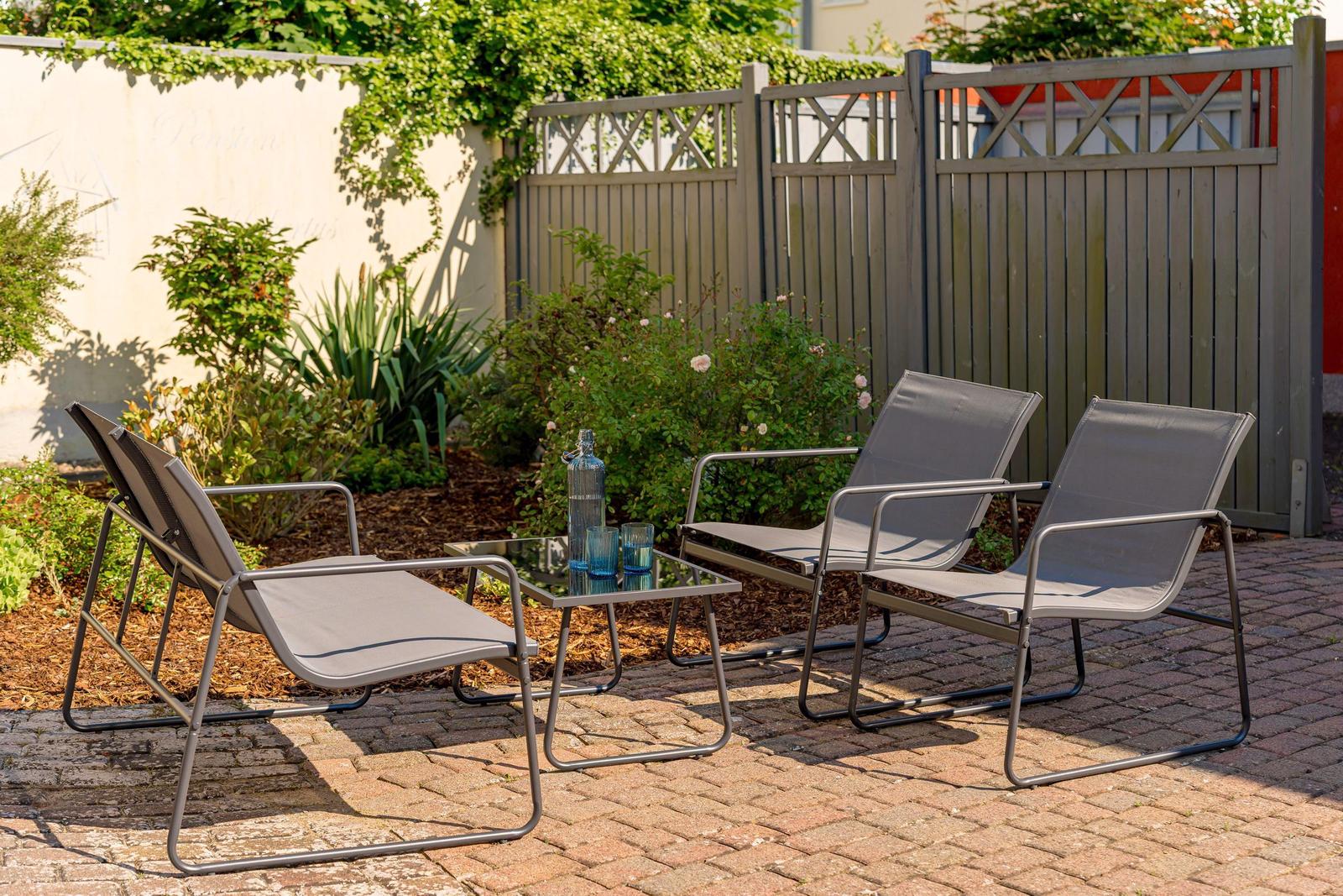 Terrasse mit drei Liegestühlen und Tisch. Hintergrund: Zaun und Grünflächen.