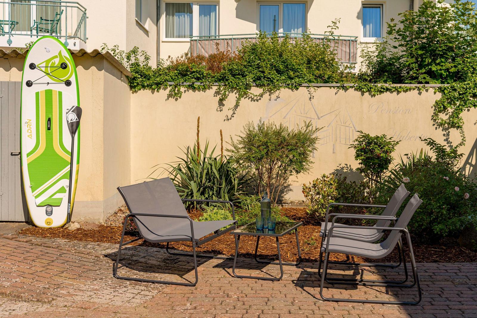 Terrasse mit Liegestühlen, Tisch und Stand-Up-Paddleboard an der Wand.
