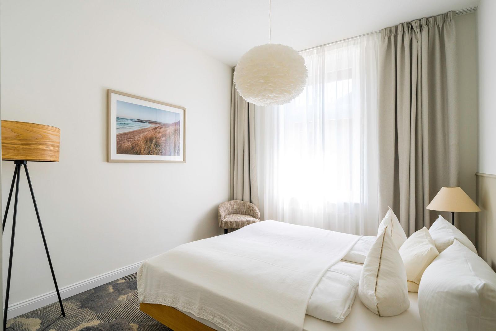 Schlafzimmer mit Bett, Stehlampe und Fenster mit Vorhängen.