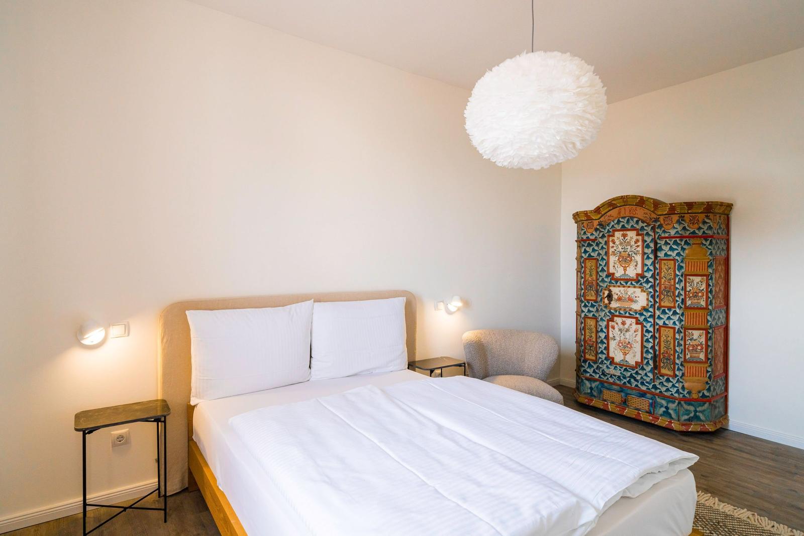 Schlafzimmer mit Bett, Nachttisch und farbenfroher Kommode.