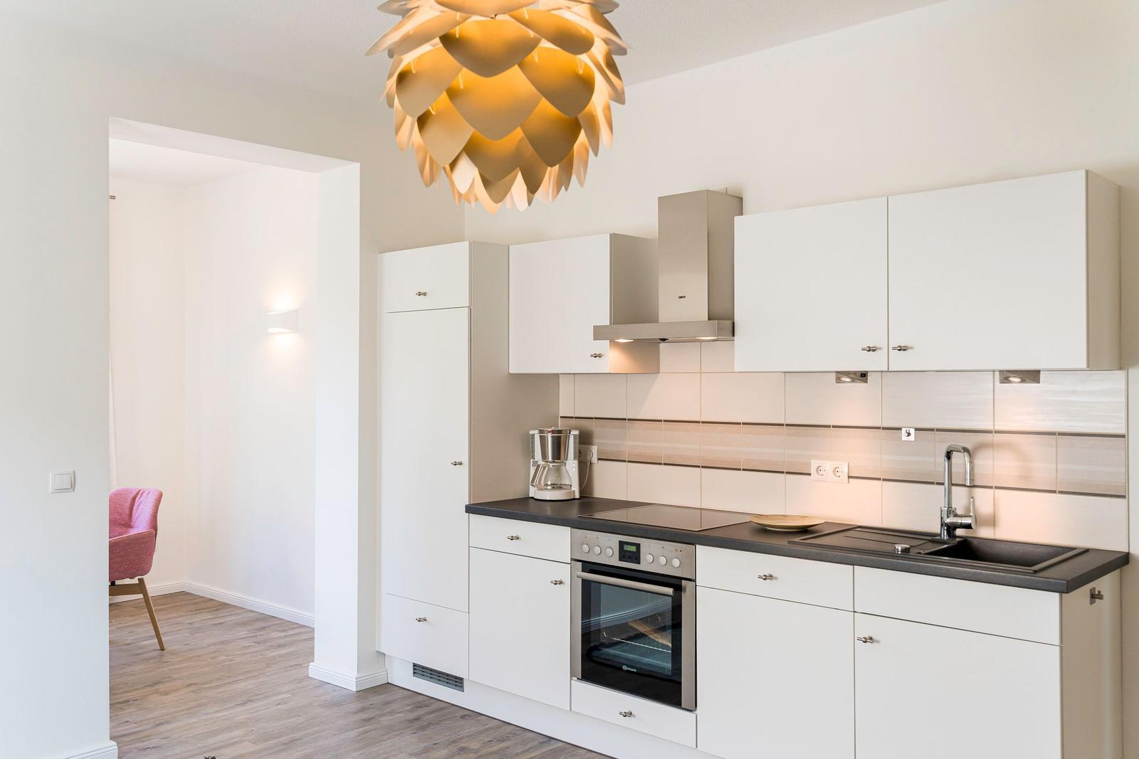 Küche mit weißen Schränken, Edelstahlspüle und moderner Deckenleuchte.