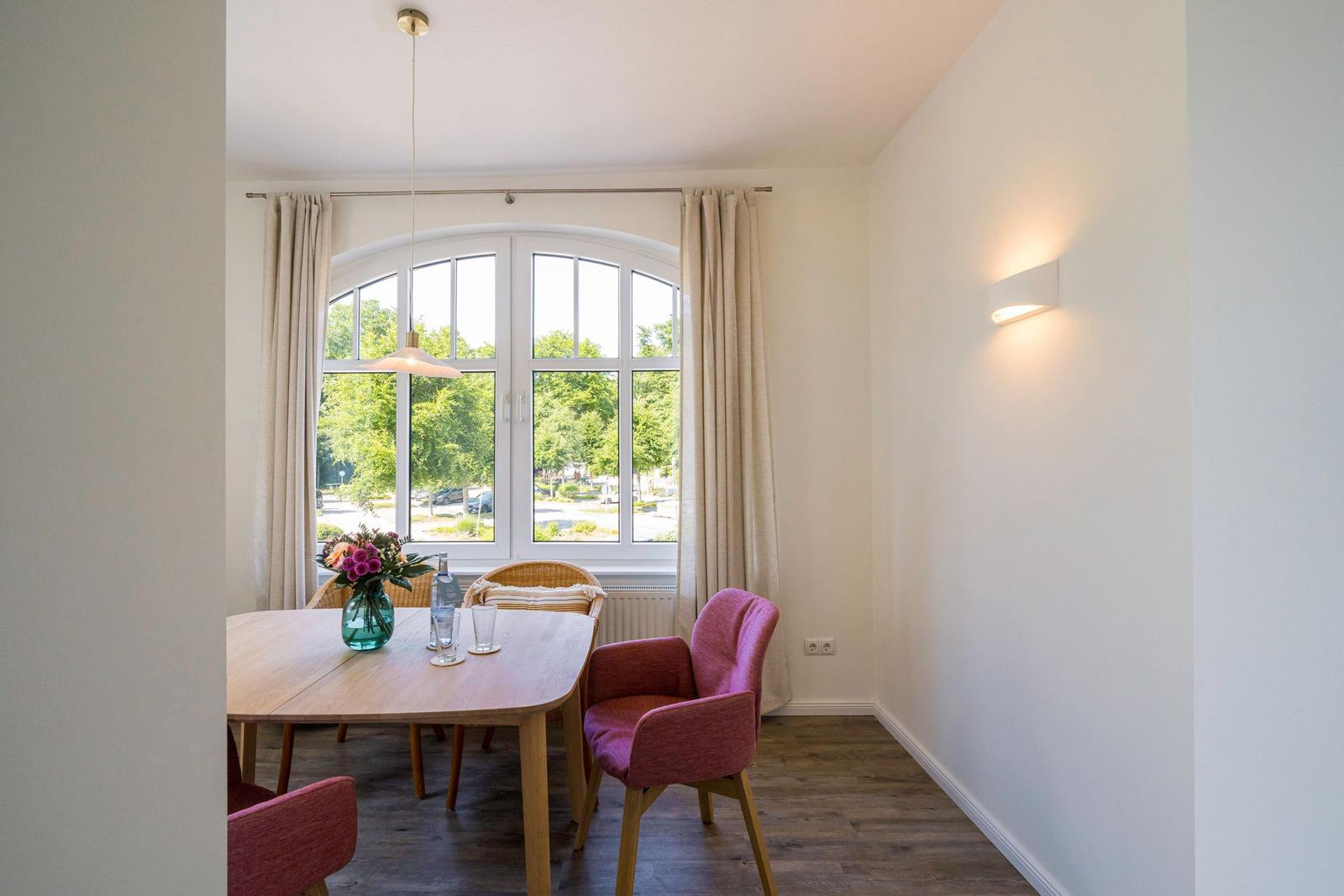 Esszimmer mit Tisch, Stühlen und großem Fenster. Blick auf grüne Bäume.