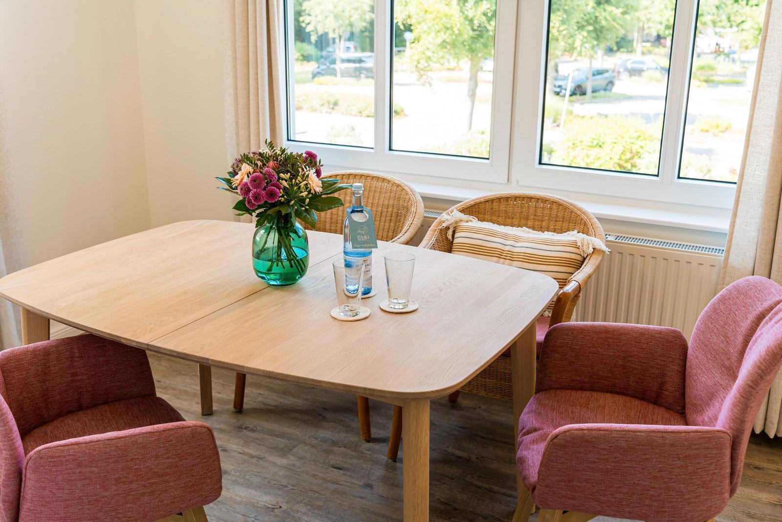 Essbereich mit Holztisch, Stühlen und Blumen am Fenster.