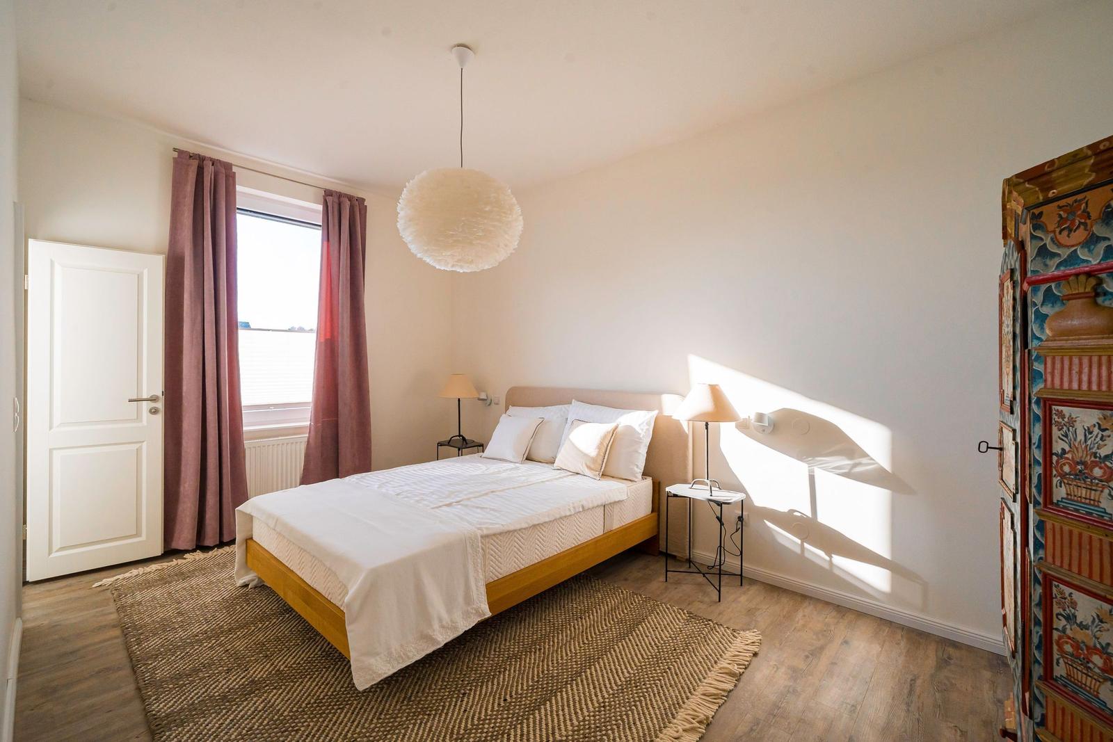 Schlafzimmer mit Bett, Fenster, Lampe und dekorativem Schrank.