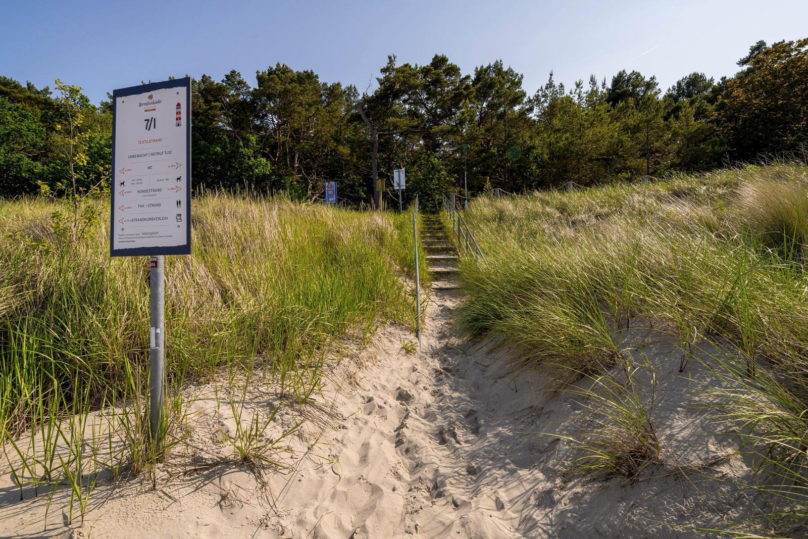 Weg zur Strandpromenade mit Schild und Stufen durch Gras und Sand