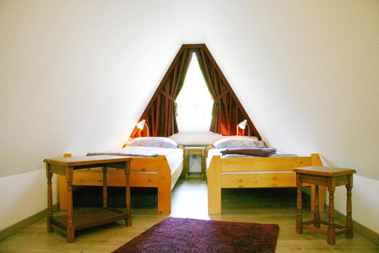 Zwei Holzbetten unter einem Dachfenster mit Vorhängen.