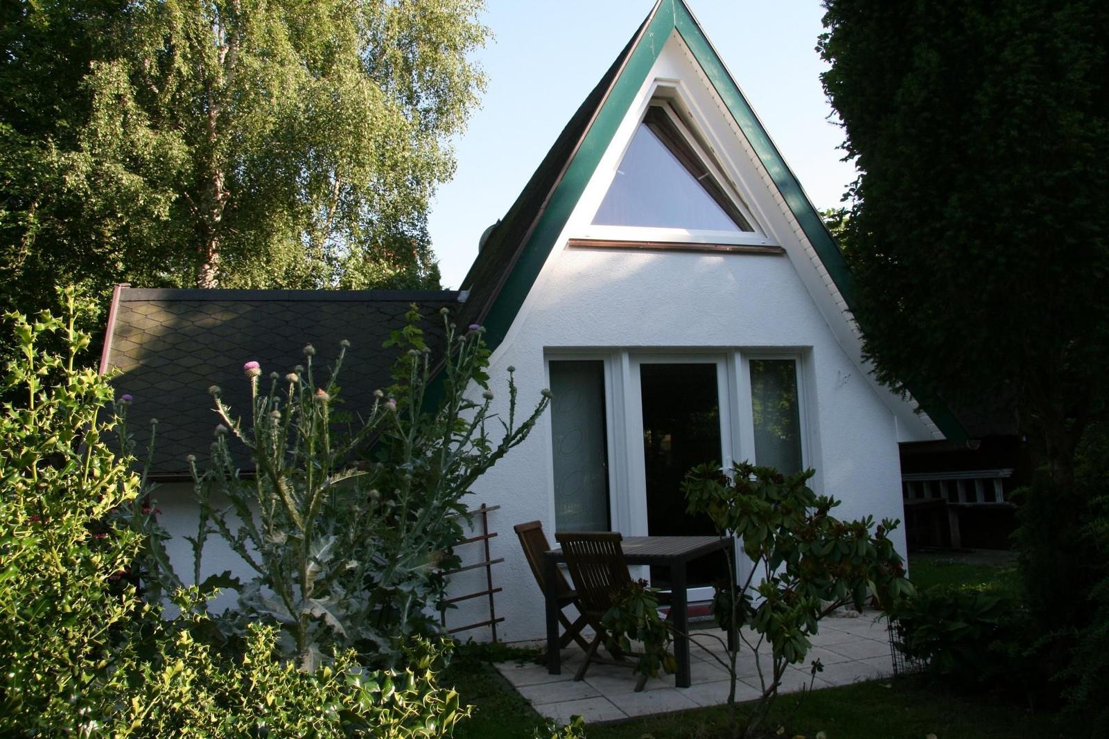 Wohnhaus mit Dreiecksfenster, Terrasse und Garten. Holztisch und Stühle vor der Tür.