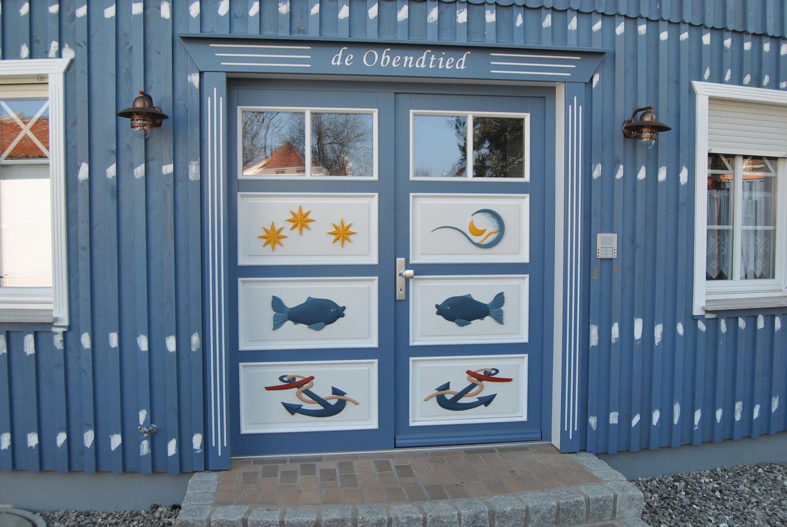Eingangstür mit Fisch- und Ankerdekoration. Blaue Holzwand mit weißen Streifen.