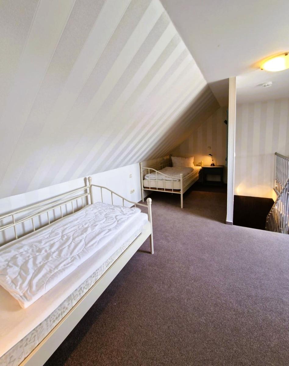 Zwei Betten in einem Dachgeschosszimmer mit gestreiften Wänden und Teppichboden.