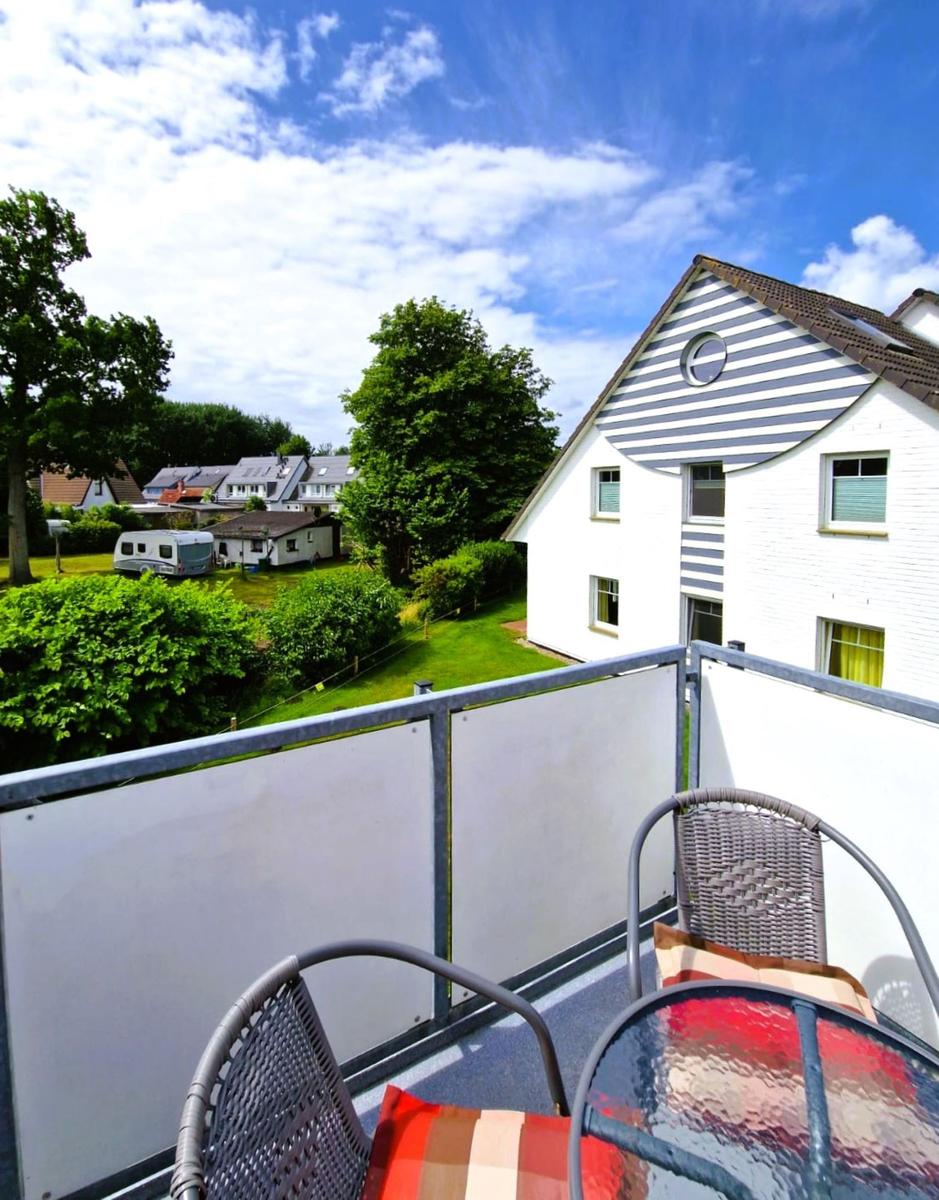 Terrasse mit Tisch und Stühlen. Blick auf grüne Wiese und Haus mit Streifenfassade.