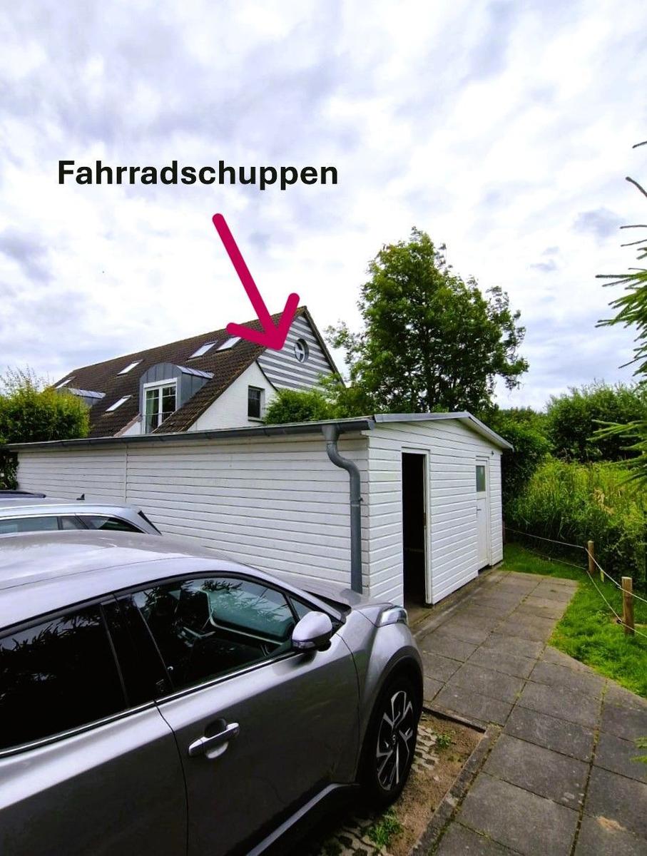 Fahrradschuppen mit Eingang und Dach. Hintergrund: Haus mit Dachfenstern.
