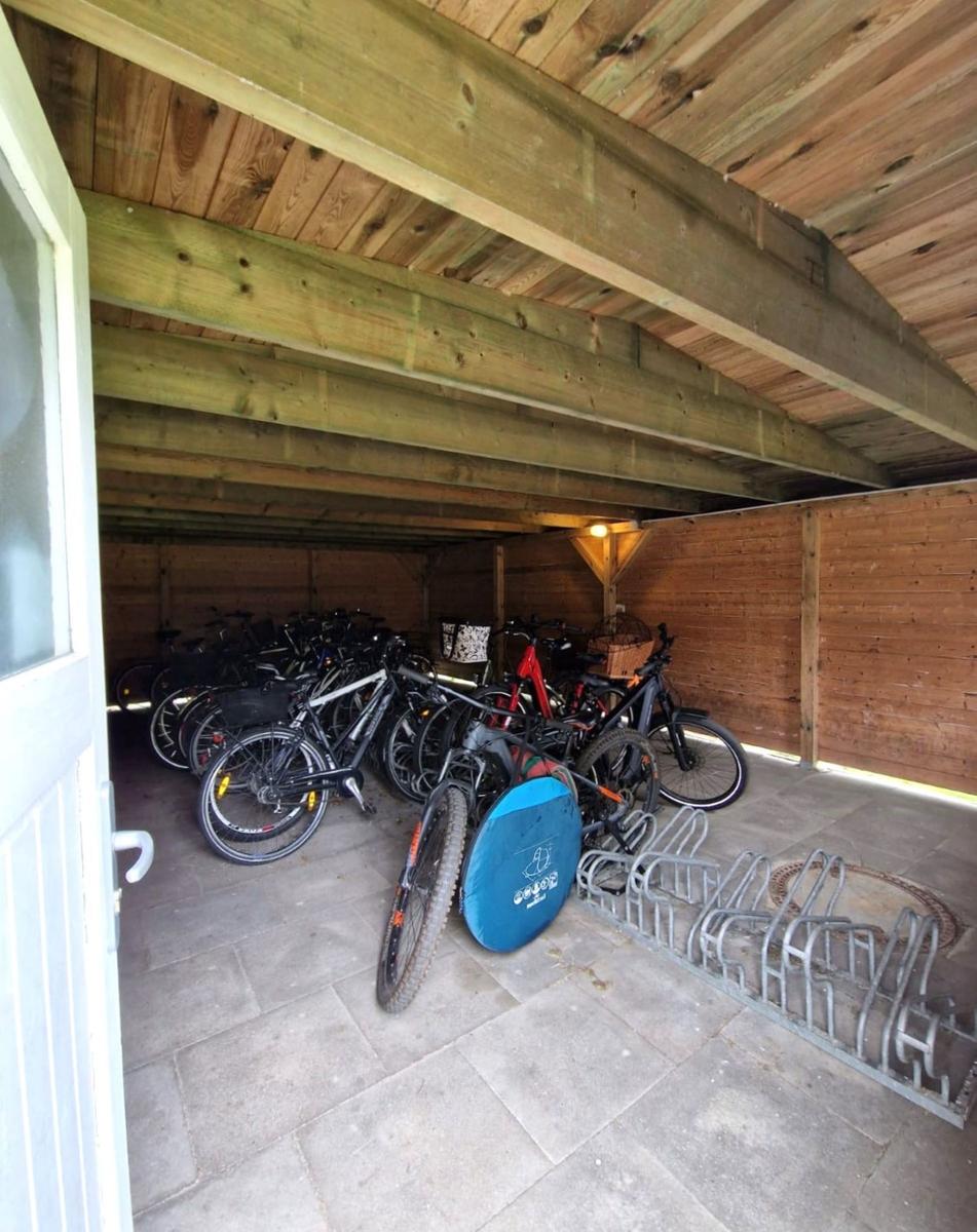 Holzüberdachter Fahrradstellplatz mit mehreren Fahrrädern und einem Fahrradständer.