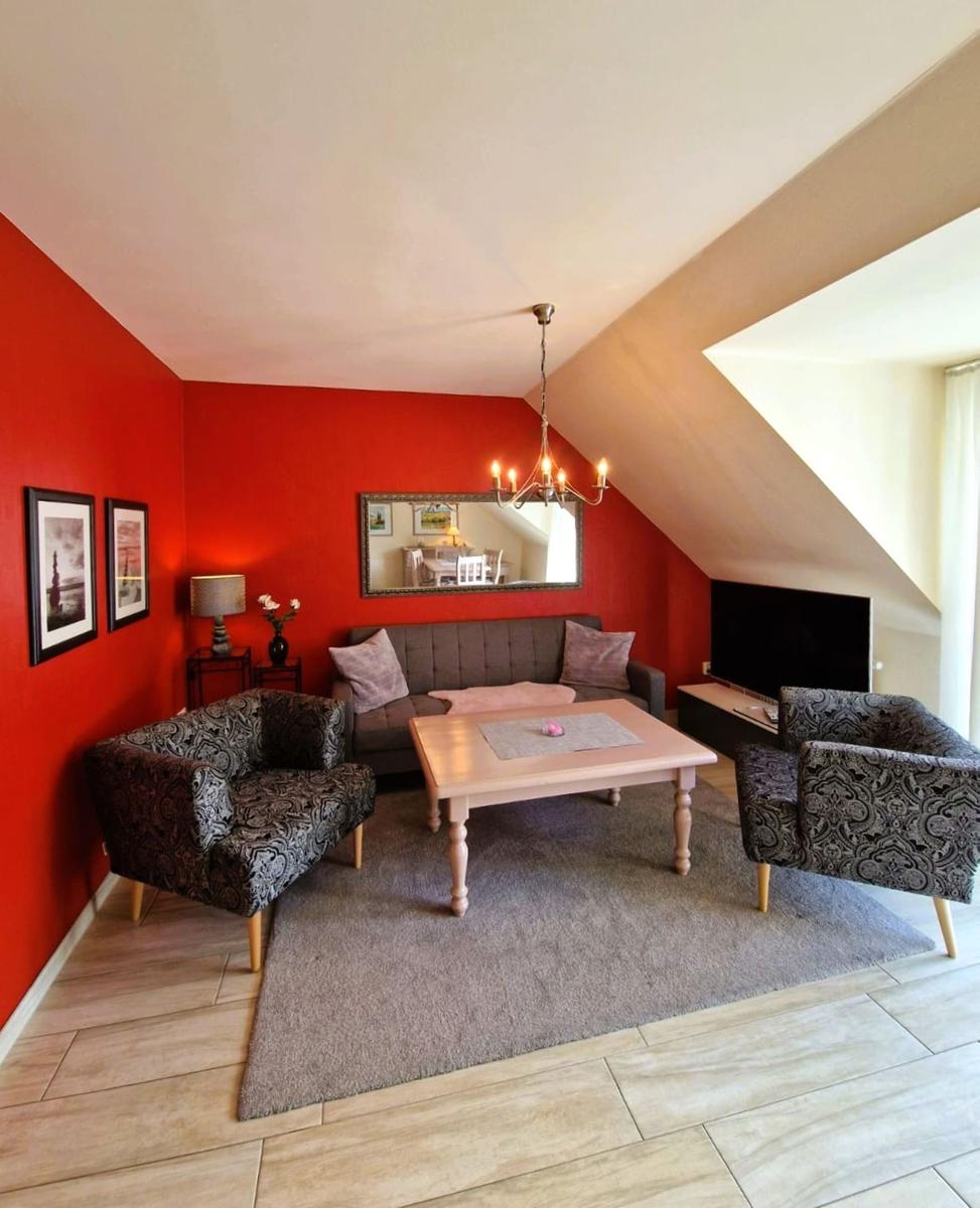 Wohnzimmer mit roten Wänden, Sofa, zwei Sessel und Fernseher.