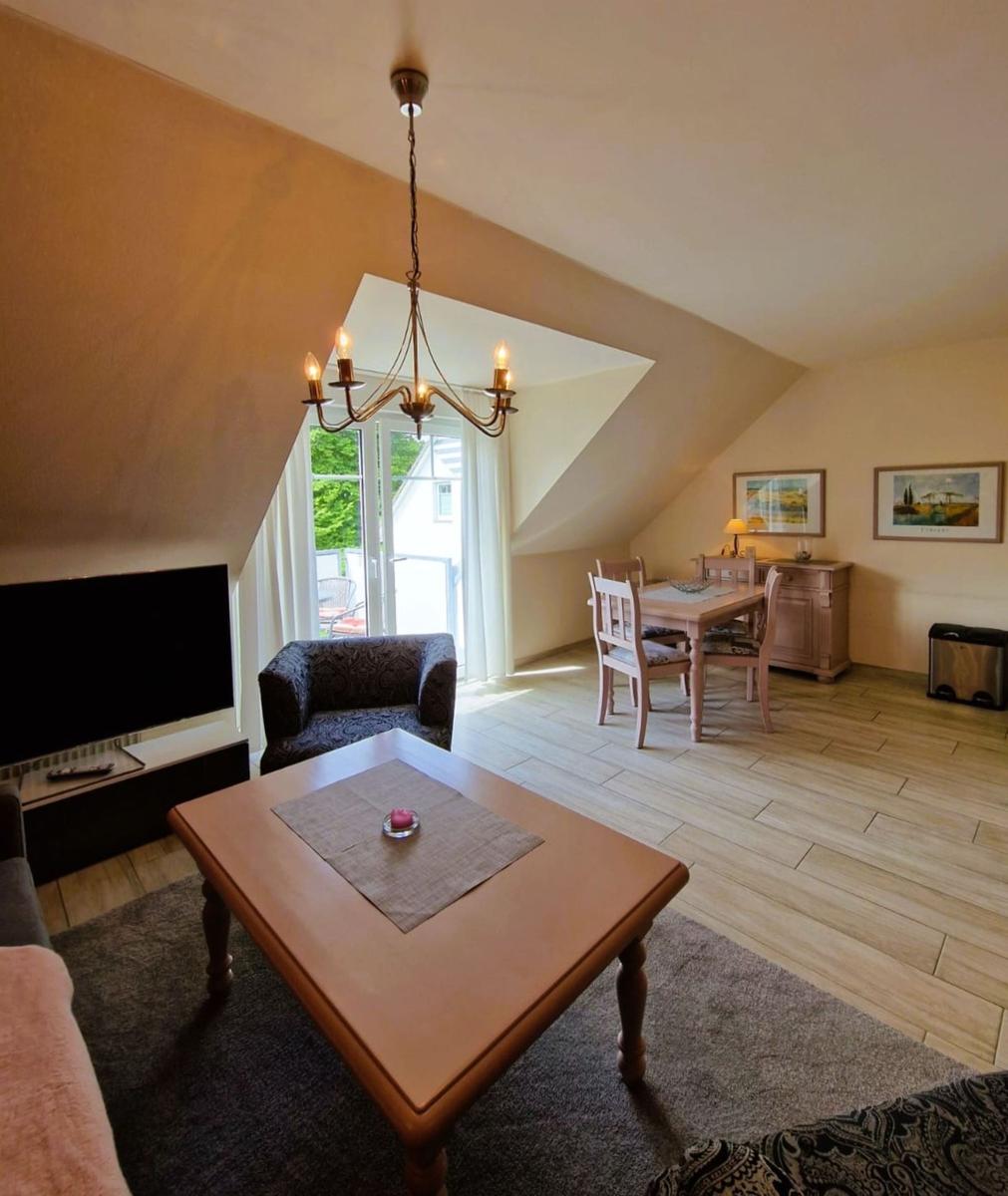 Wohn- und Essbereich mit TV, Tisch, Stühlen und Balkonzugang.