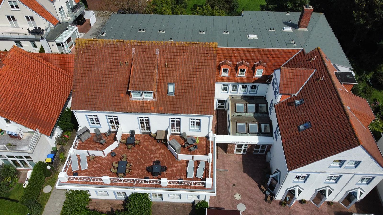 Haus mit Terrasse, Garten und rotem Dach. Mehrere Sitzgelegenheiten und Tische.