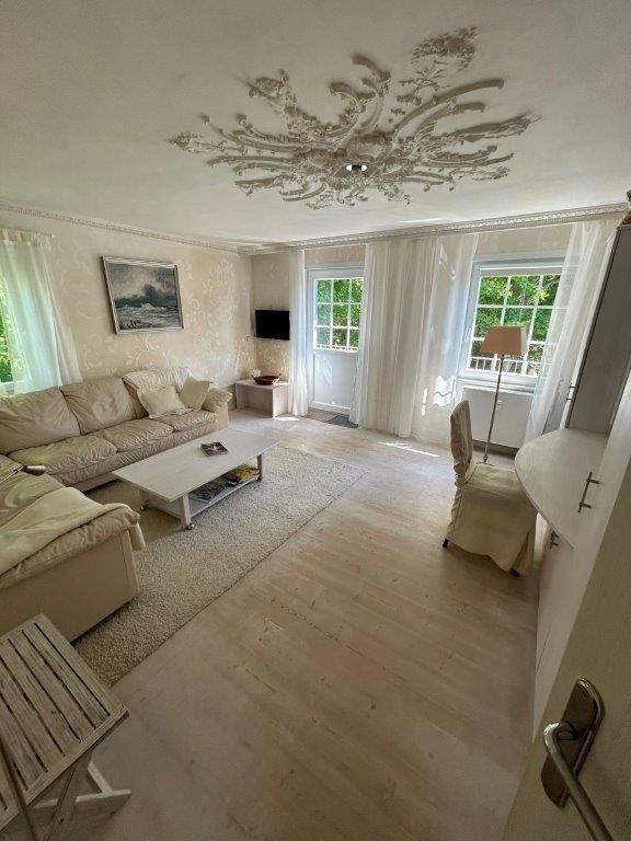 Wohnzimmer mit Sofa, Couchtisch und Fenstern mit weißen Vorhängen.