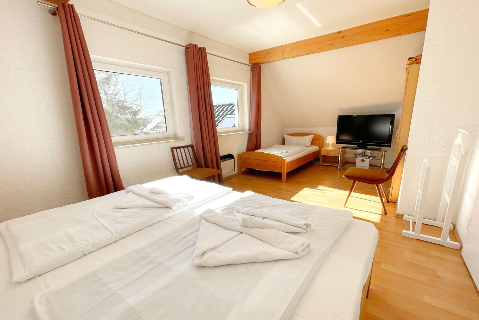 Zimmer mit Doppelbett, Einzelbett, TV und Holzboden.