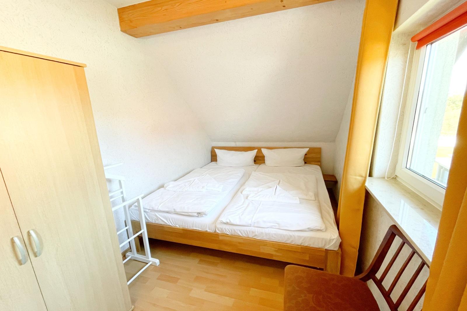 Zimmer mit Doppelbett, Kleiderschrank und Fenster. Holzboden und Deckenbalken.