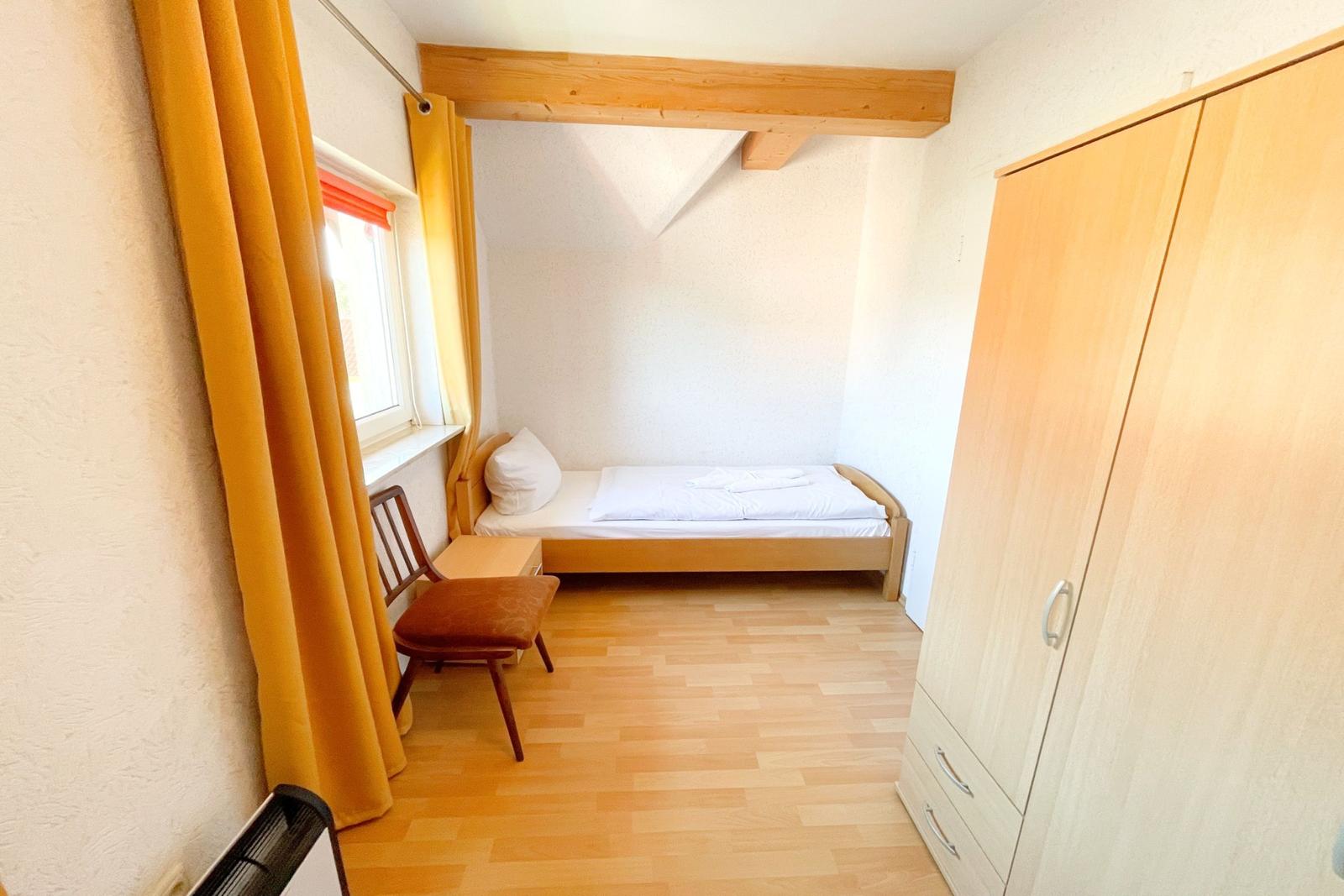 Ein Schlafzimmer mit einem Bett, einem Kleiderschrank und einem Stuhl vor einem Fenster.