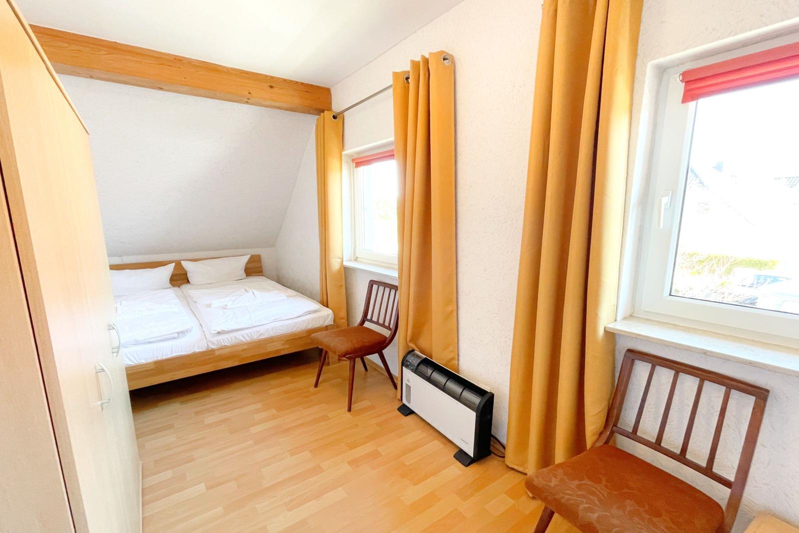 Doppelbettzimmer mit Holzboden, zwei Stühlen und Fenstern mit Vorhängen.